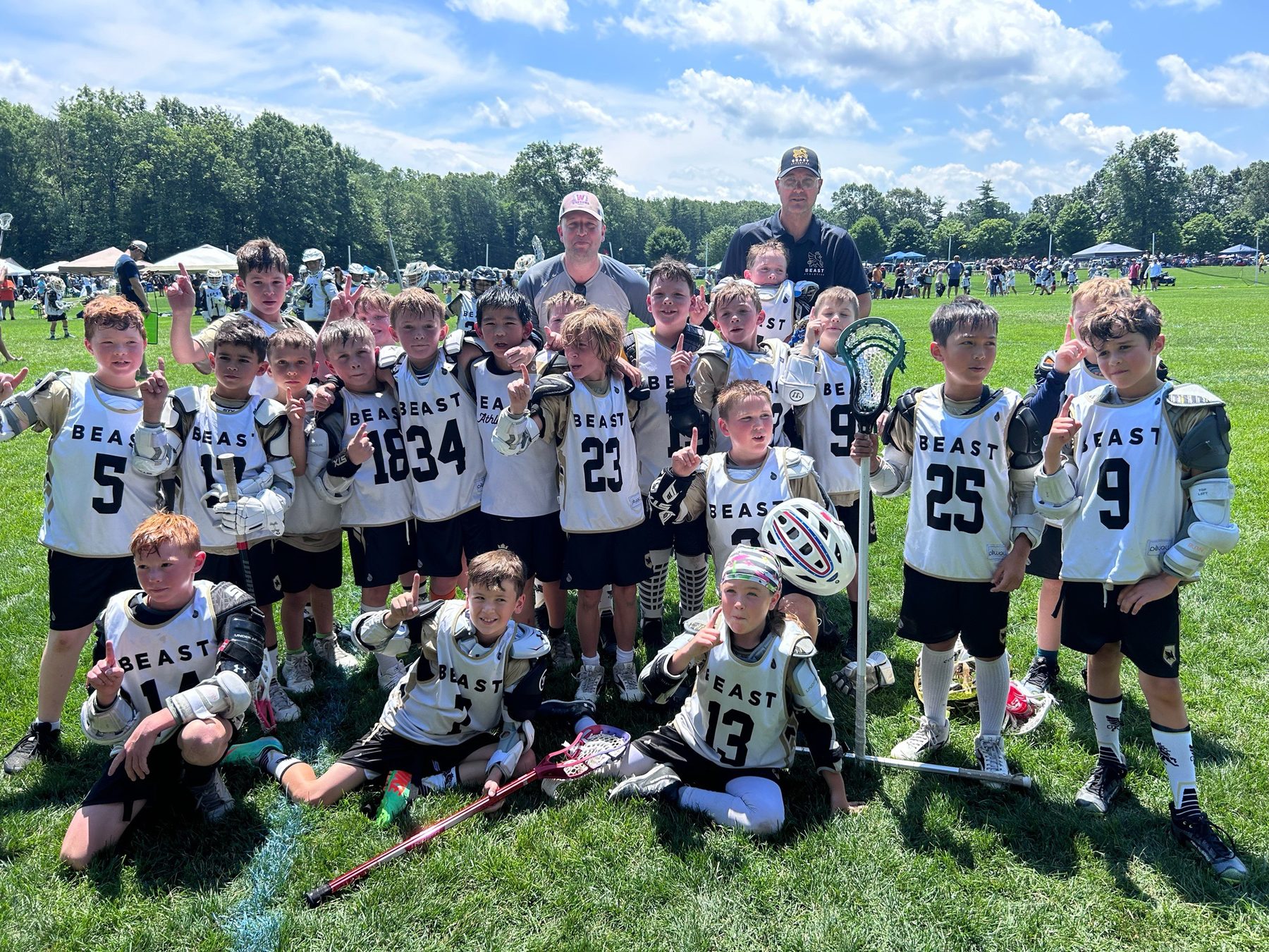 A young BEAST team in white pinnies holding up number-one fingers with their coaches at a U.S. tournament