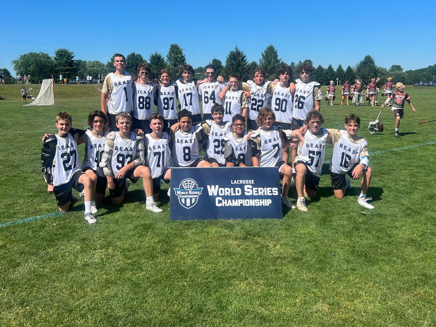 A BEAST team in white pinnies posing behind a Lacrosse World Series Championship sign